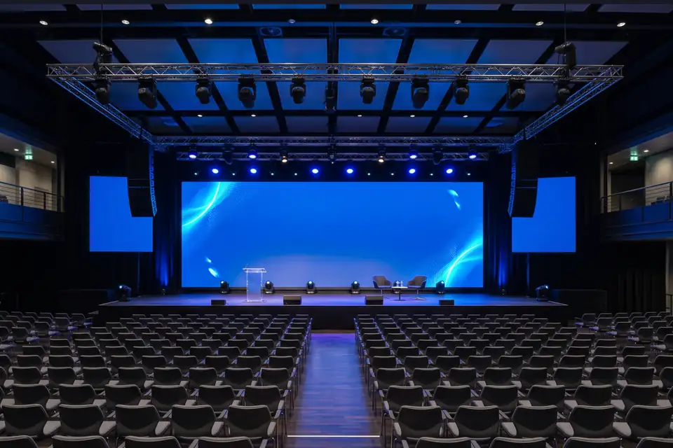 Illustration: an auditorium with a wide LED wall, side screens and moving lights on truss